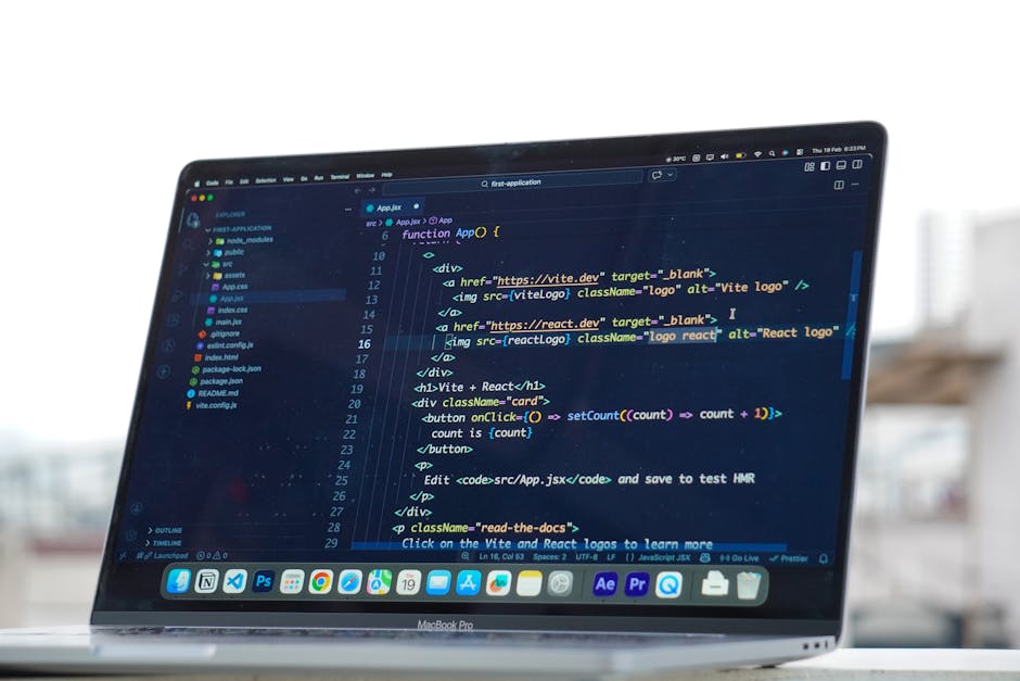 Close-up of a MacBook Pro laptop screen displaying a dark-themed software development environment with lines of code, including HTML and JavaScript snippets, inside a room with large windows. The lapt