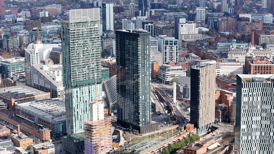 A high-angle black-and-white photograph of a city skyline showing a densely built urban area with various modern and older buildings. In the foreground, several multi-storey office buildings and resid
